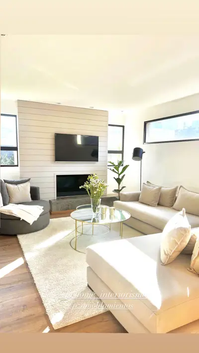 Living con sillones claros, mesa ratona de vidrio y grandes ventanales.
